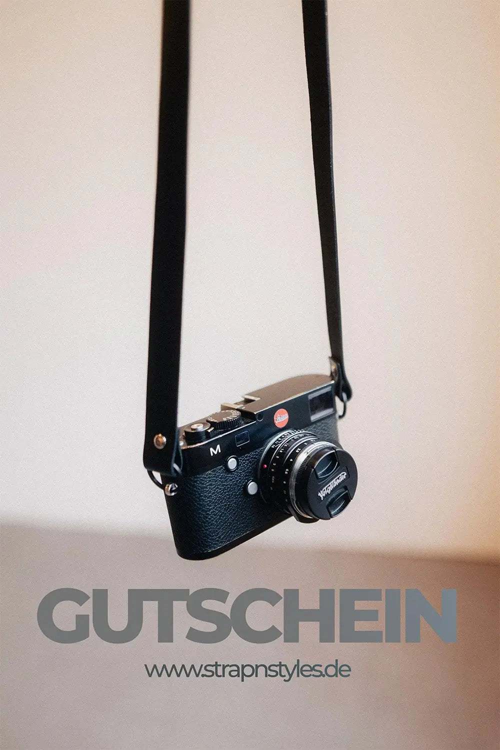 Vintage camera hanging on a black strap with the word Gutschein and website URL strapnstyles.de below, representing a digital voucher for photography accessories.