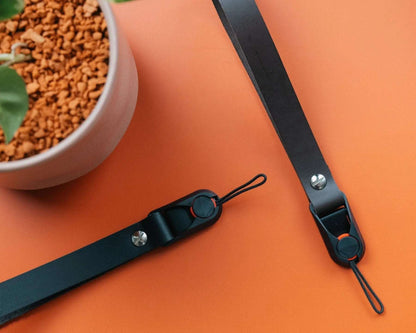 Short black leather quick release camera wrist straps on orange background near plant pot