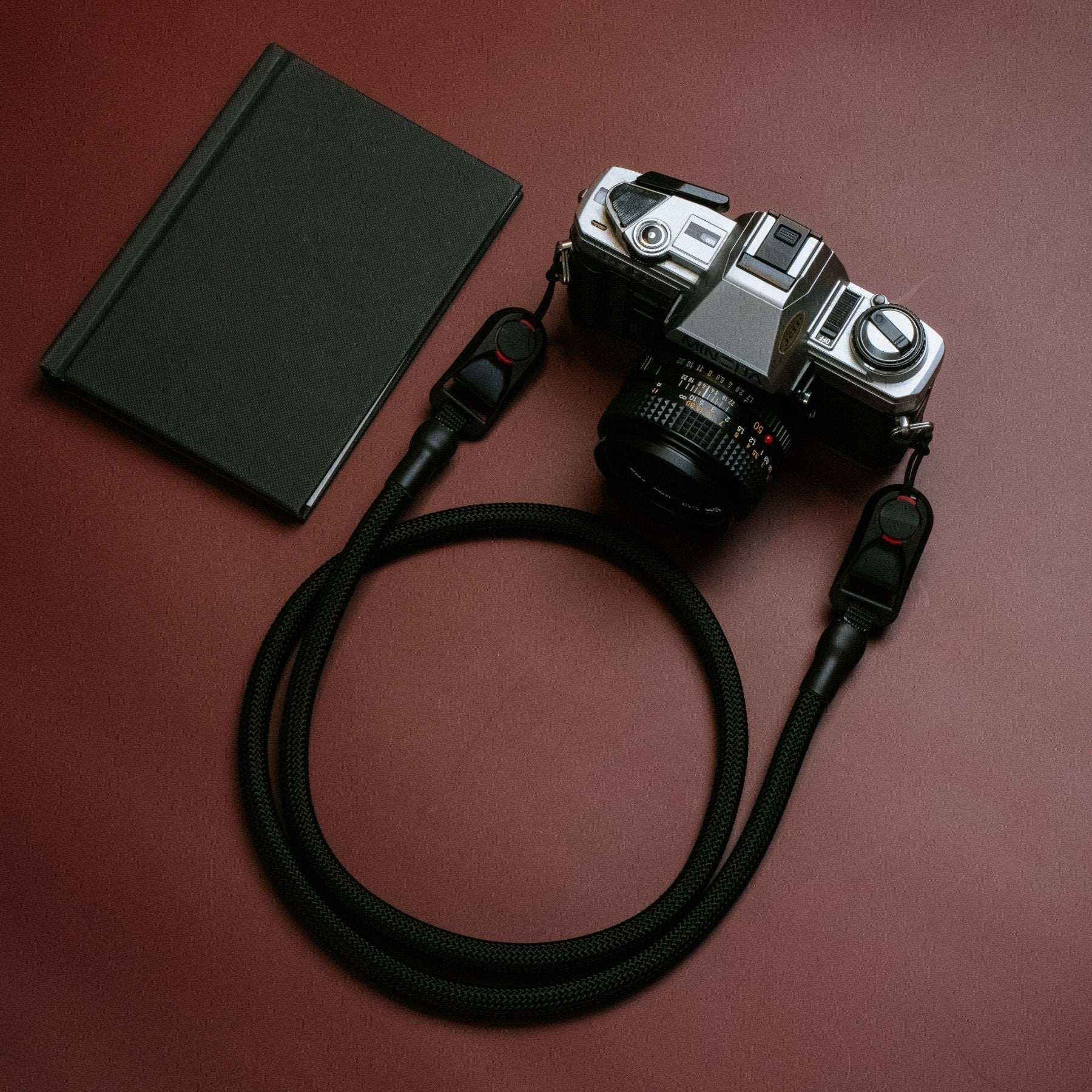 Quick Release Kameragurt vintage camera rope strap with durable black polypropylene climbing rope and quick-release adapters attached to an analog camera on a brown background next to a black notebook