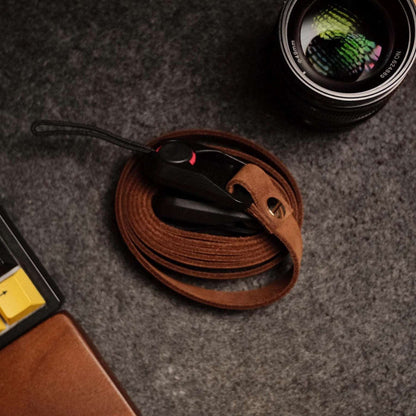 Quick release brown leather camera strap coiled next to camera lens and keyboard
